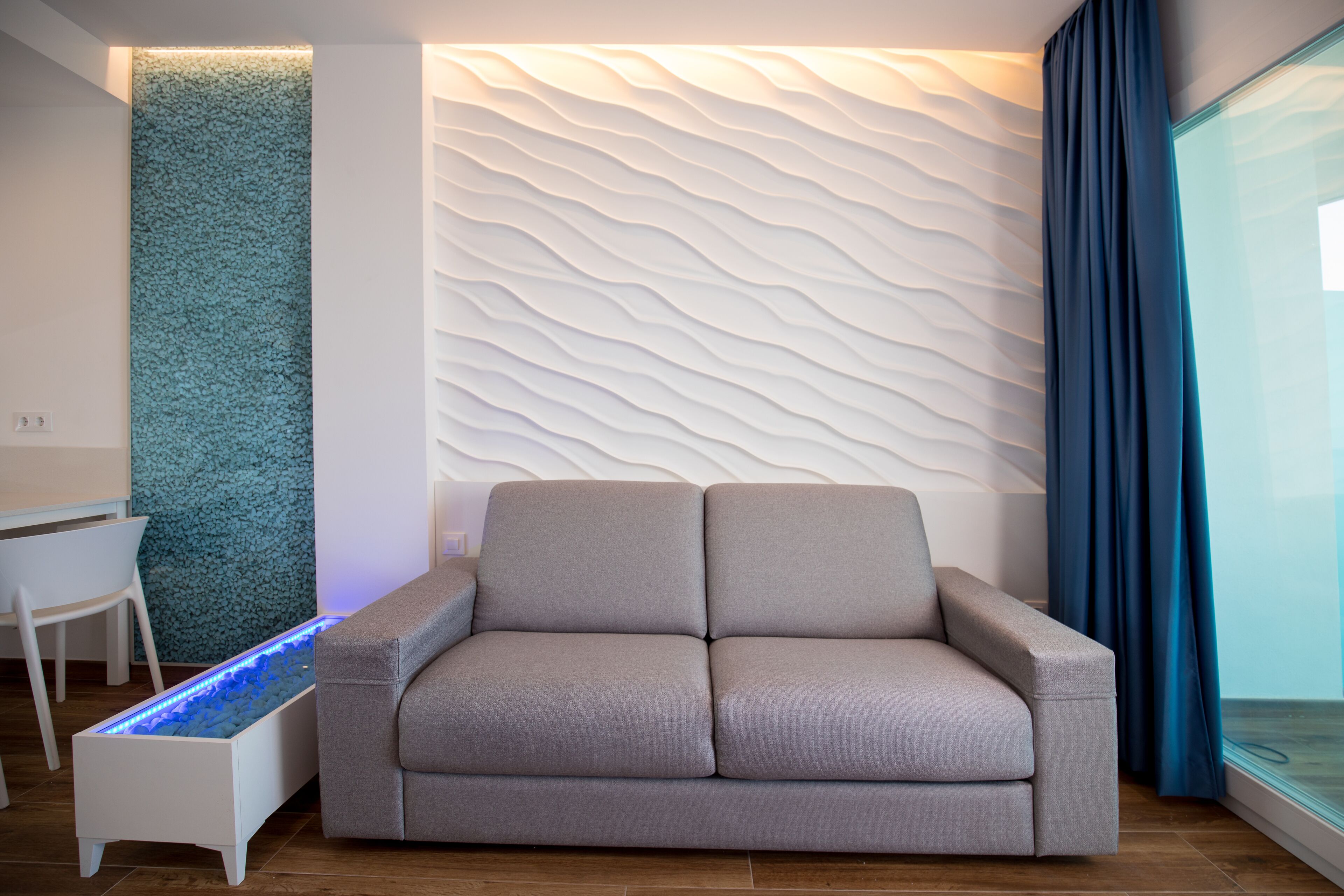 A modern living room with a sofa, a white wall with a textured pattern, a blue accent wall, and a glass partition.