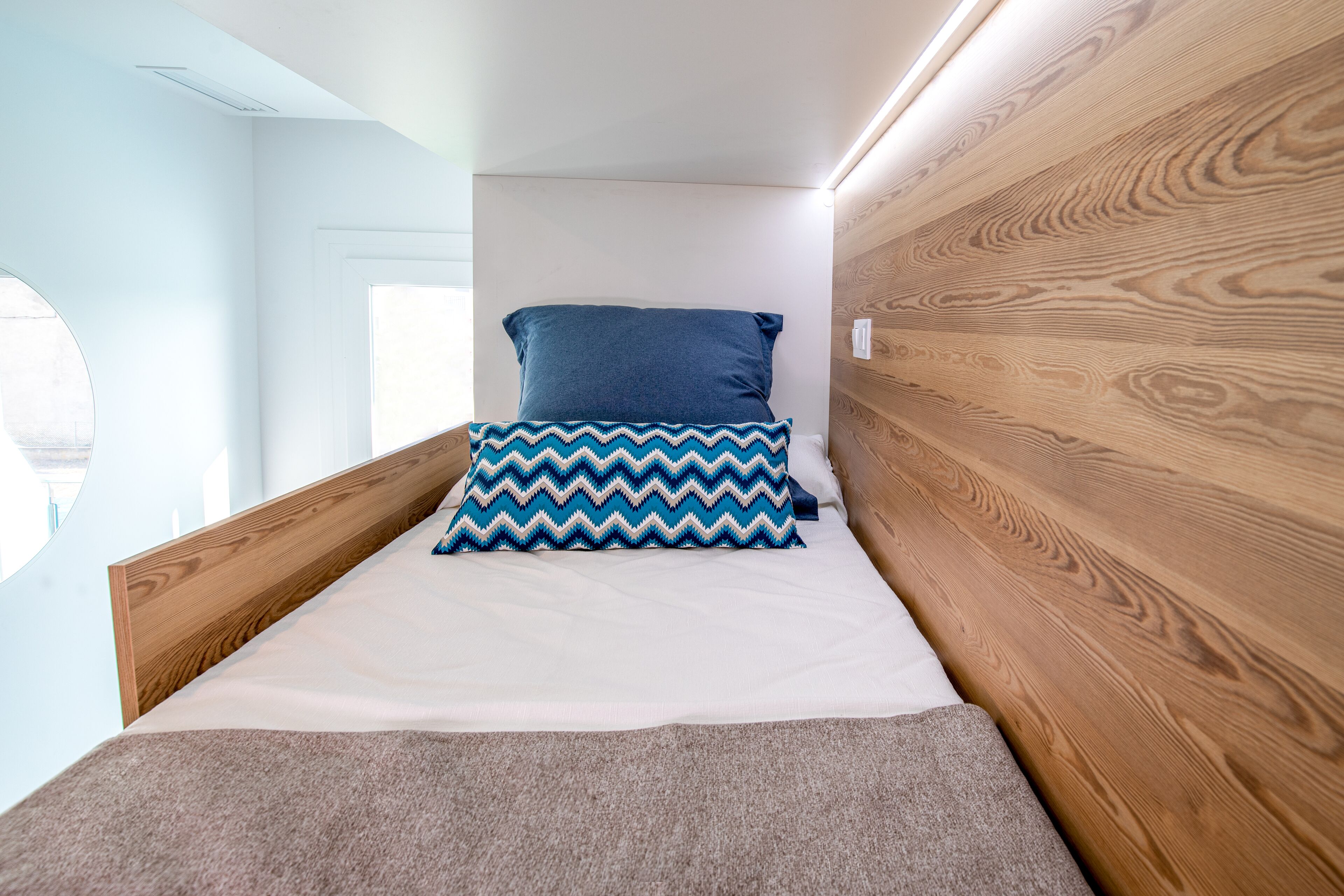 Una cama compacta con cabecera de madera, almohada estampada y colchón blanco liso.