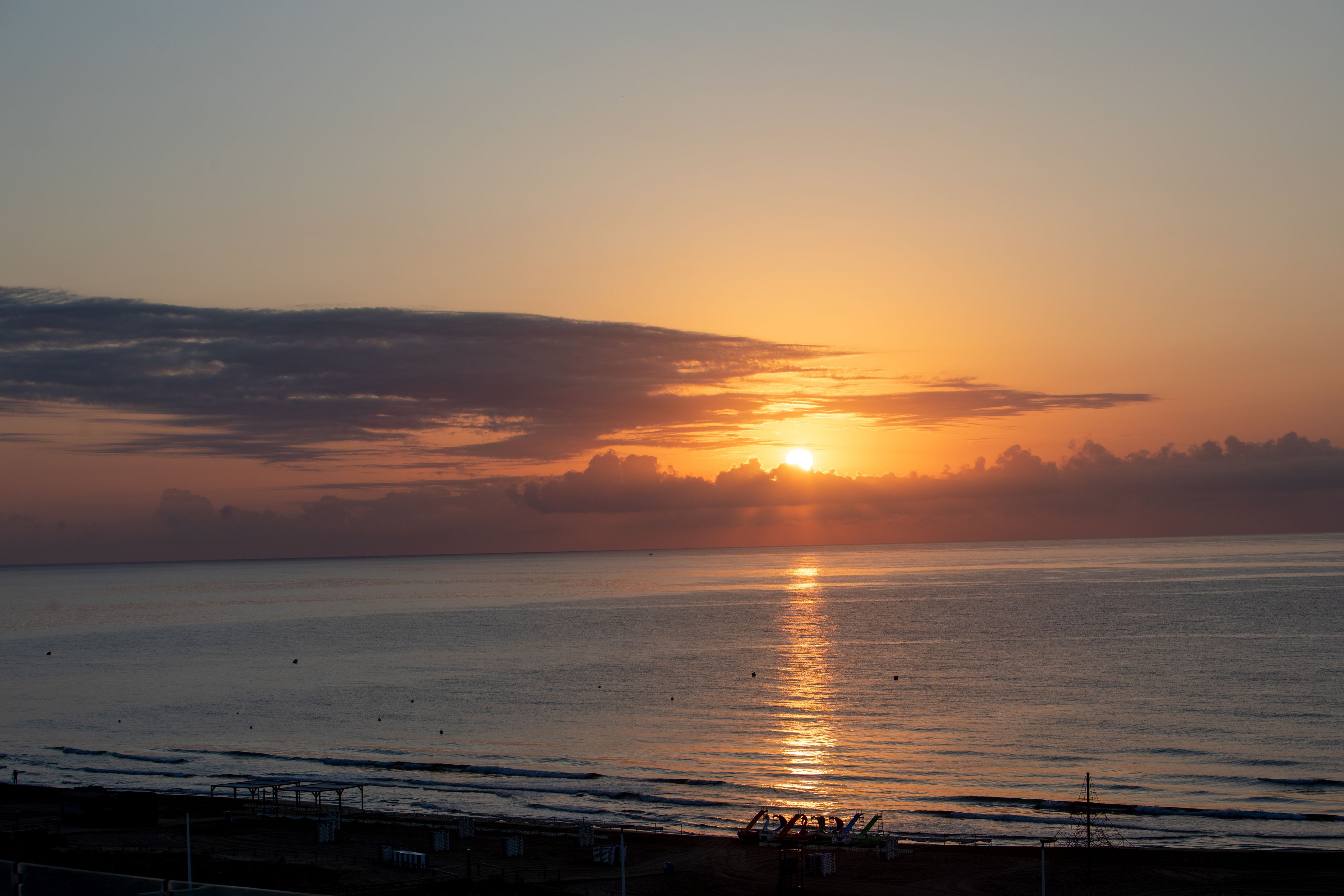 A sunset over a calm sea with a beach in the foreground.