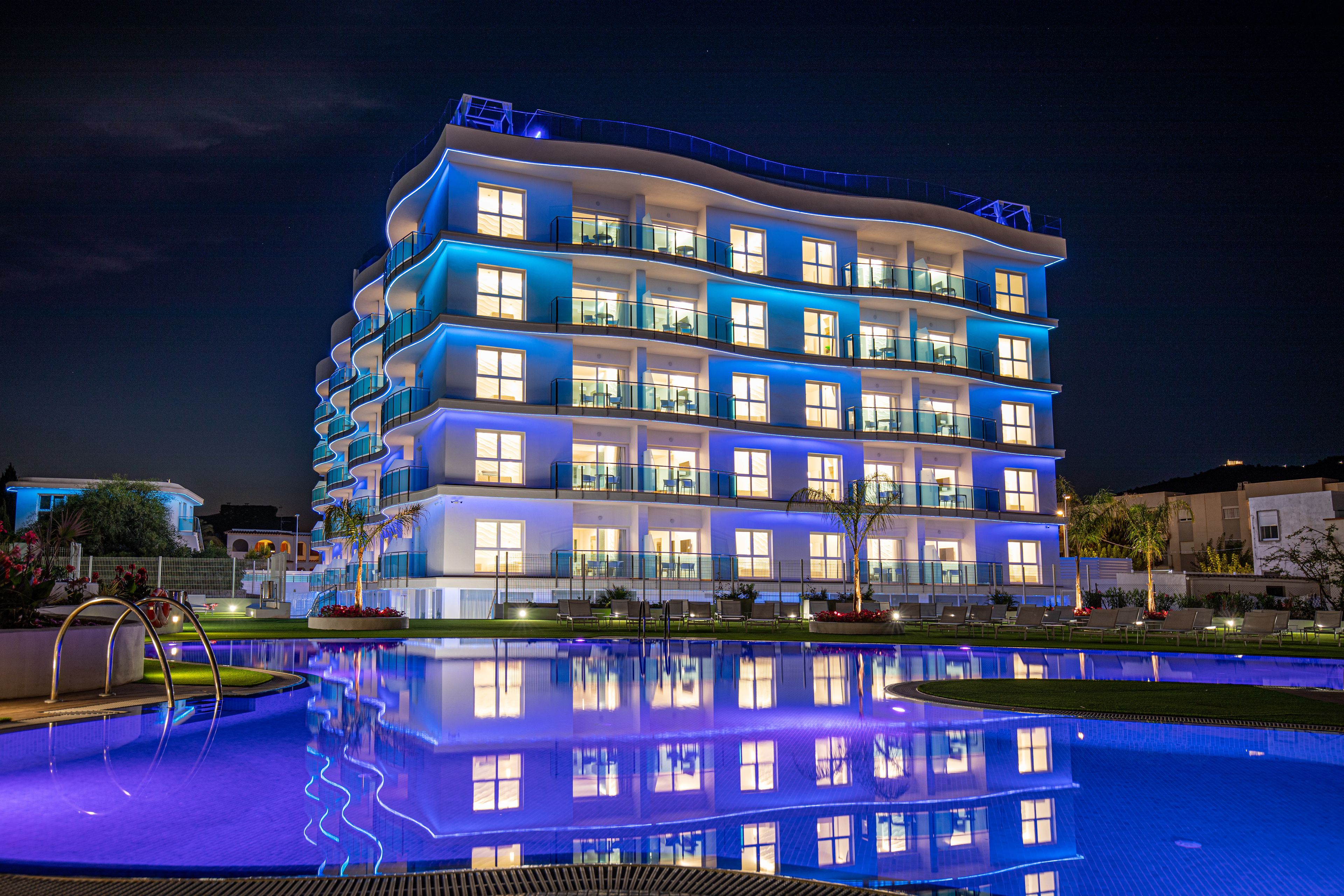 Un hotel de varios pisos con balcones, piscina e iluminación destacada en la fachada.