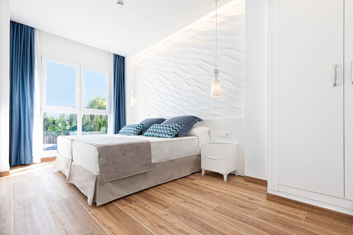 Un dormitorio moderno con una cama grande, una mesita de noche y vistas al verdor por la ventana.