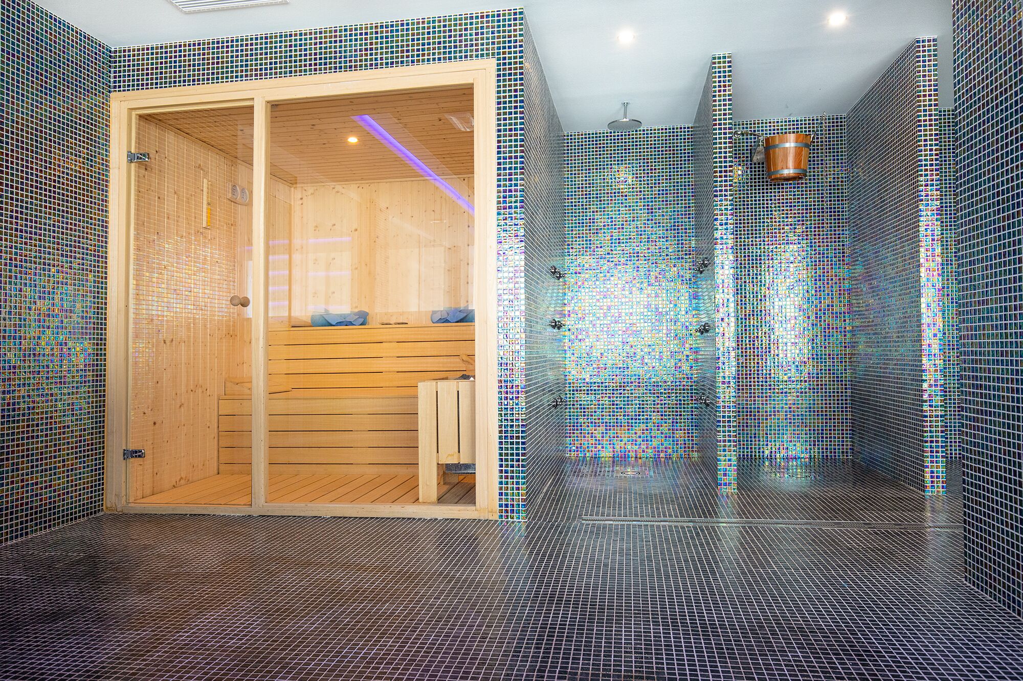 Eine Sauna mit Holzbänken und einer Glaseinfassung, umgeben von mosaikverkleideten Wänden und Boden.