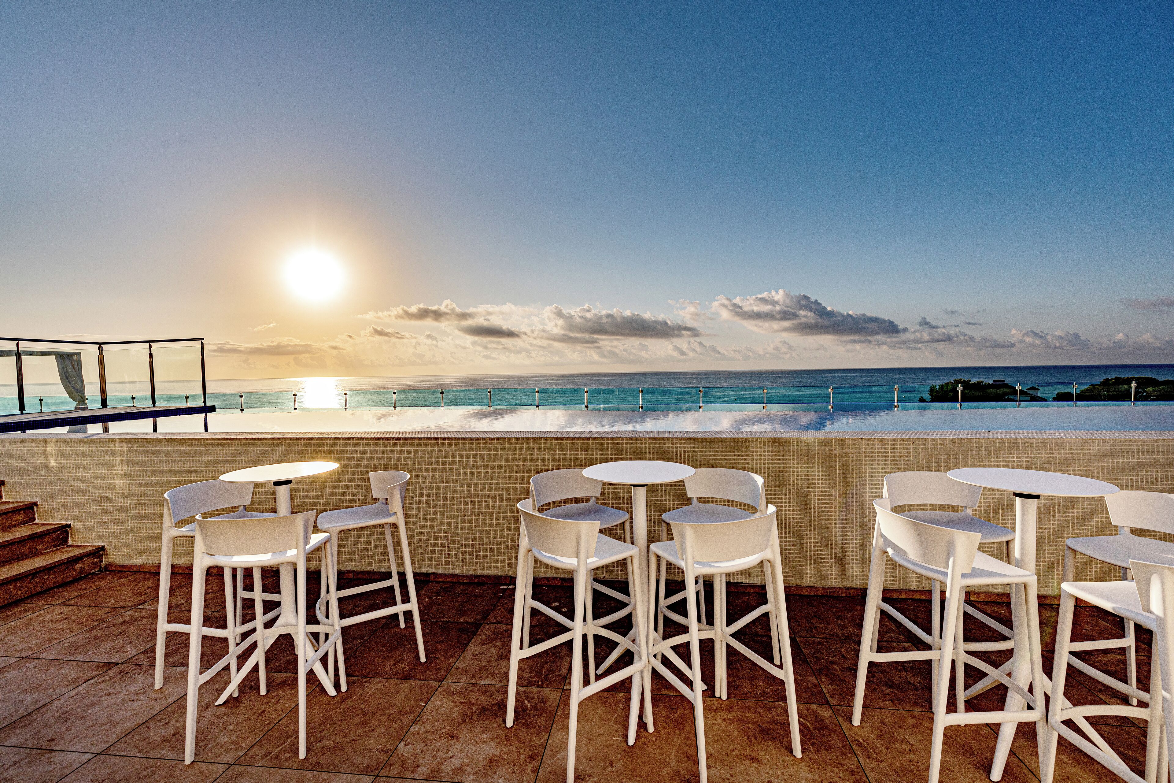 Una terraza con sillas y mesas blancas, con vistas al océano, donde se ve el mar y el cielo.