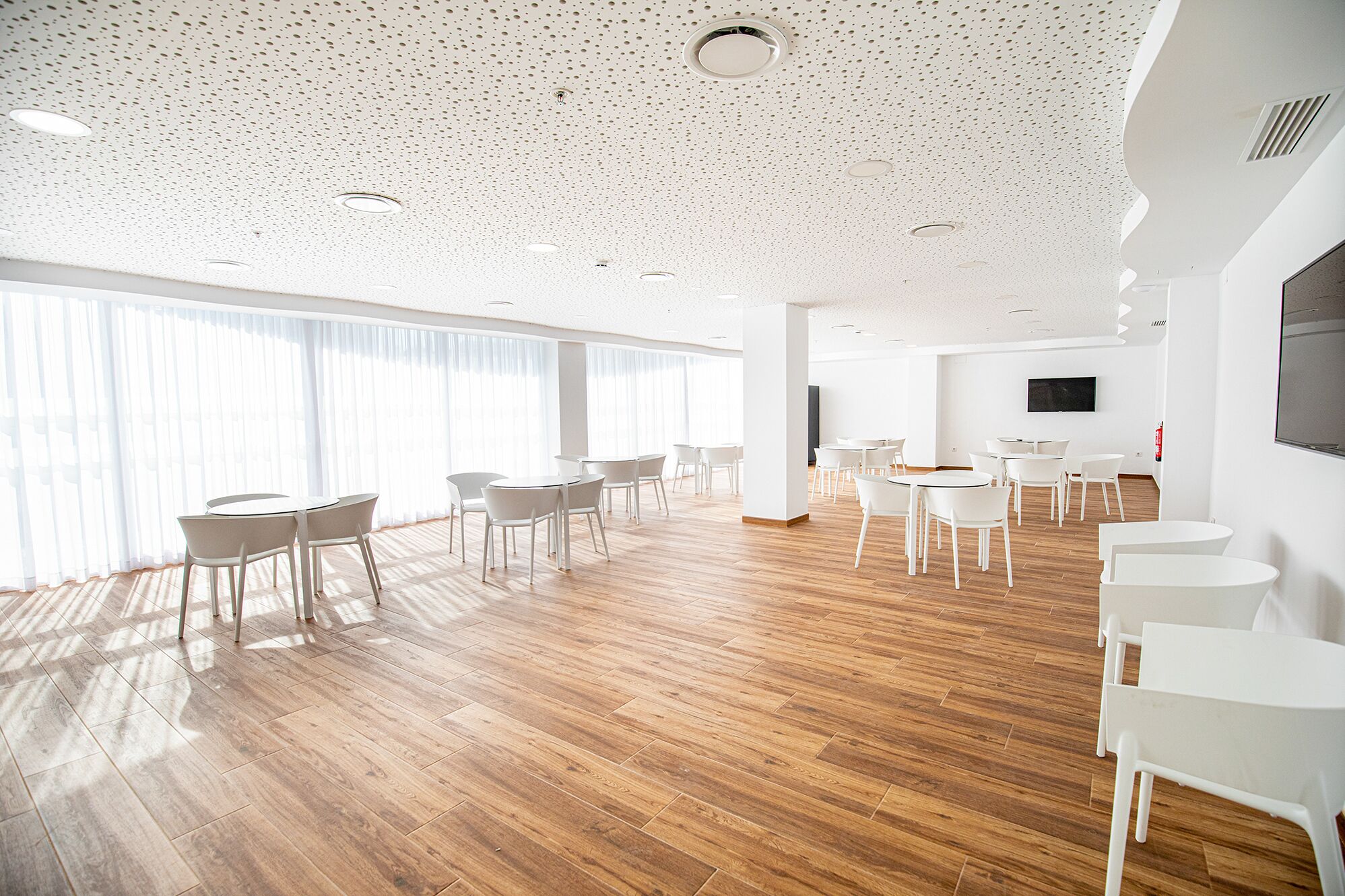 Una amplia sala de conferencias con mobiliario blanco, ventanas grandes y suelo de madera.