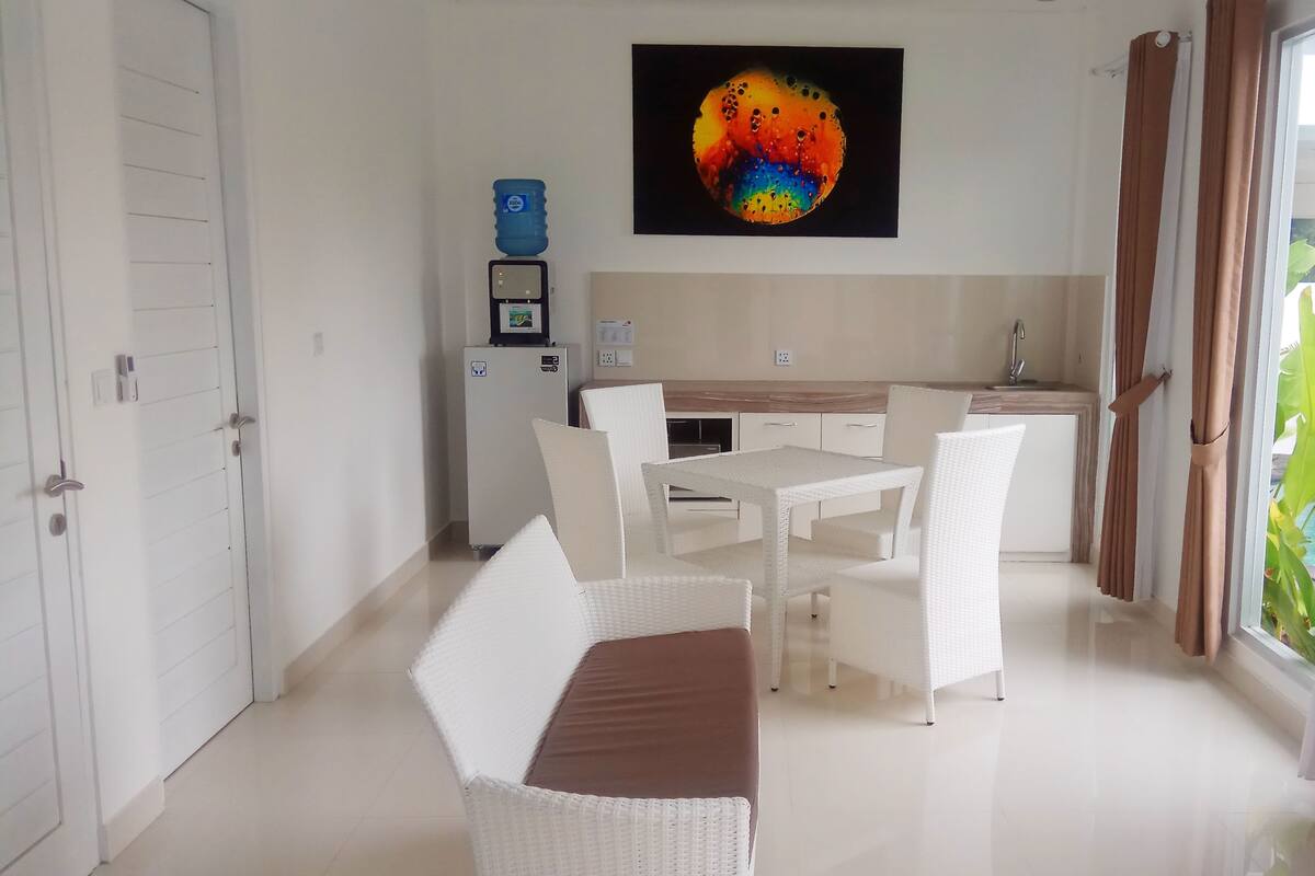 Una cocina moderna con electrodomésticos blancos, un comedor con sillas y mesa blancos, y un ventanal con cortinas.