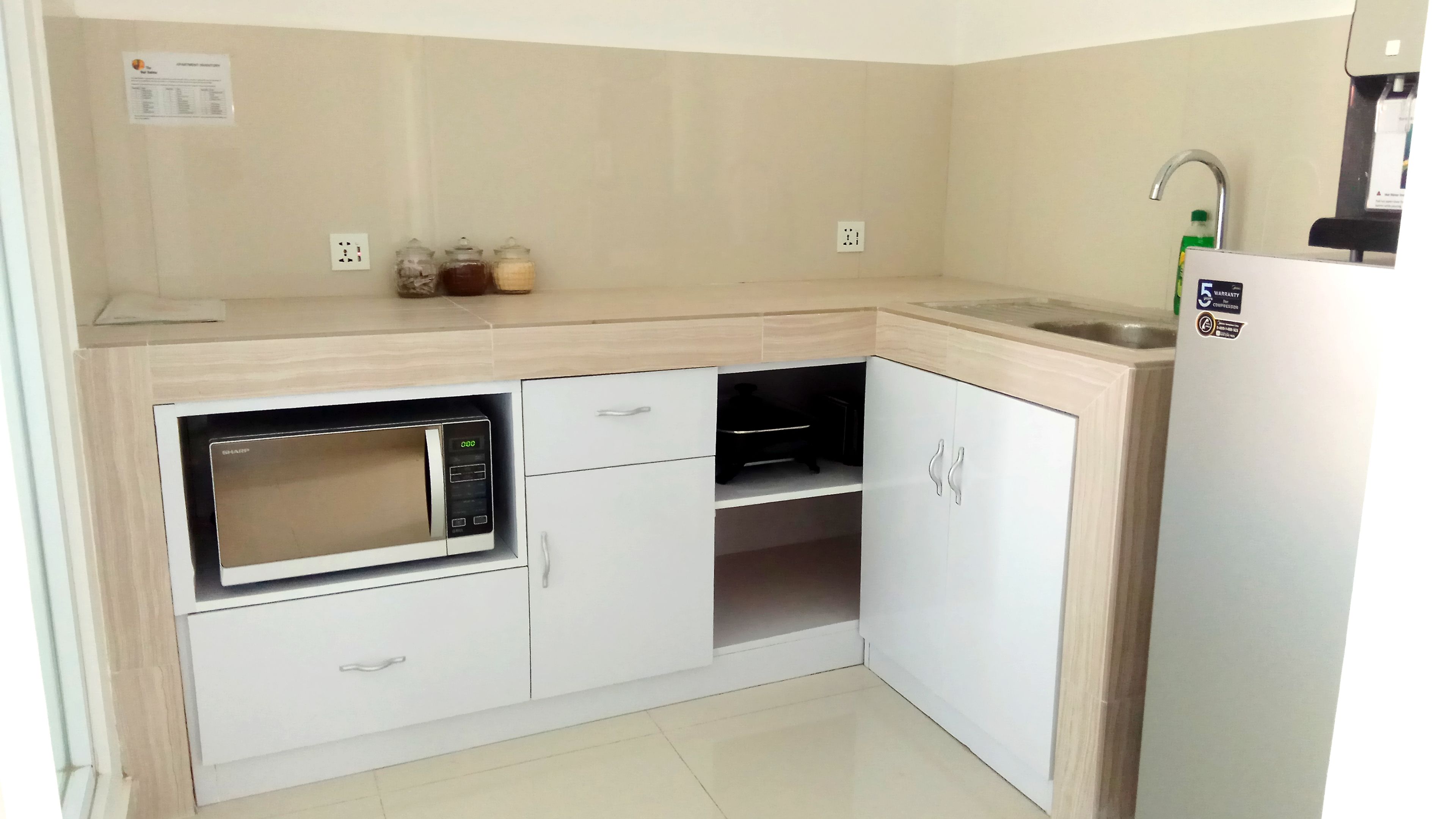 A compact kitchen with a built-in microwave, white cabinets, a sink, and a refrigerator.
