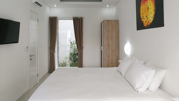 A modern hotel room with a large bed, a wardrobe, a TV mounted on the wall, and a window with curtains. - The Bali Bubble (Denpasar)