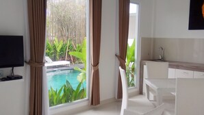 Quarto moderno com TV, área de refeições e vista para uma piscina.