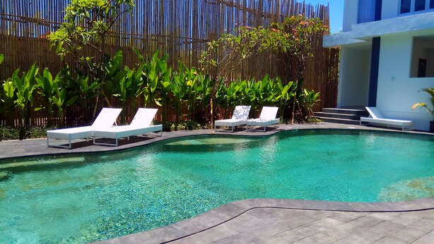 Piscina com água cristalina, rodeada por uma cerca de bambu e cadeiras de descanso brancas.