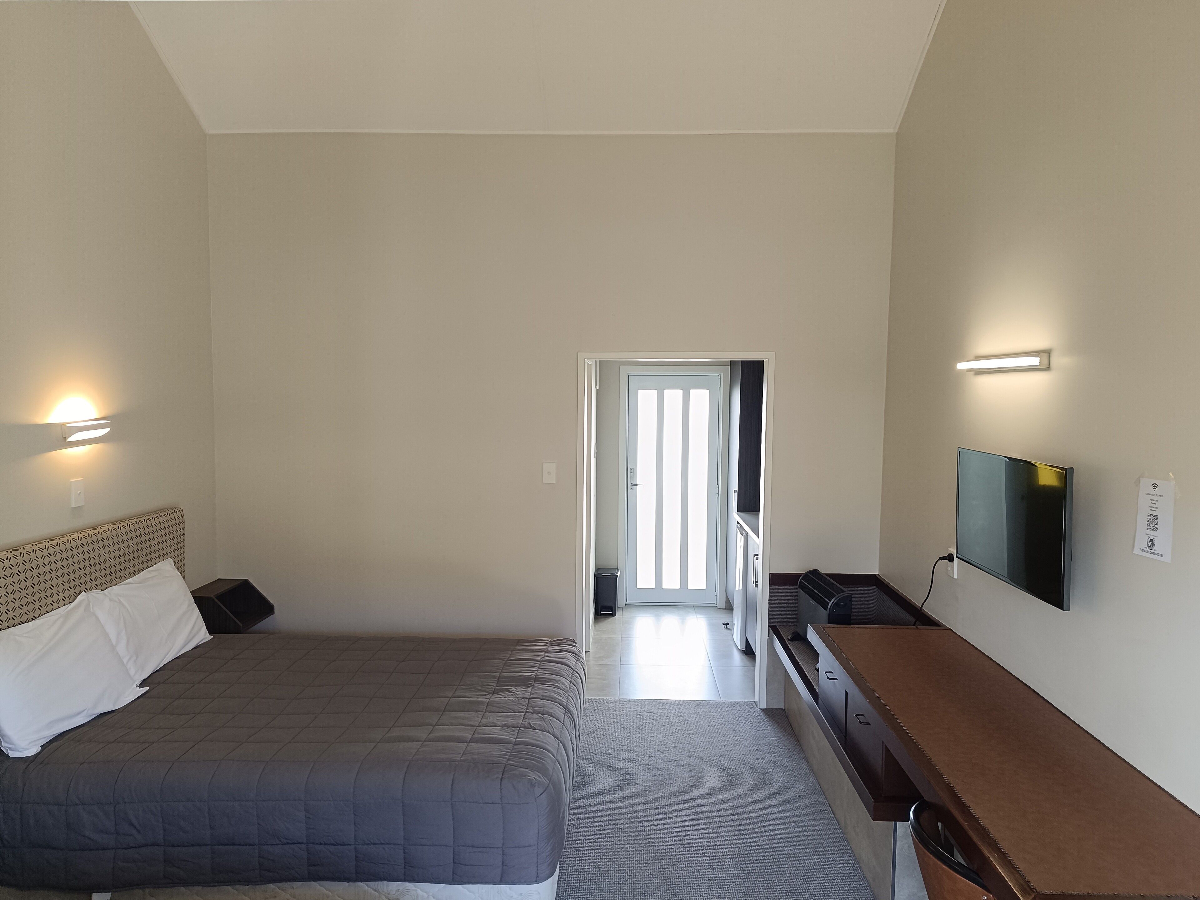 A bedroom with a bed, bedside table, TV, and a door leading to another room.