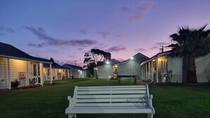 A row of motel buildings with a grassy lawn and a bench in the foreground.
