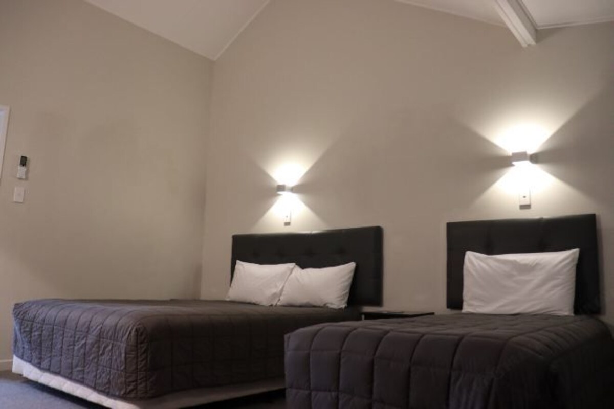 A hotel room with two beds, each with a dark headboard and white pillows, and two wall-mounted light fixtures.