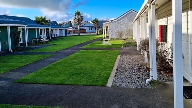 A row of single-story buildings with a well-maintained lawn and gravel pathway.