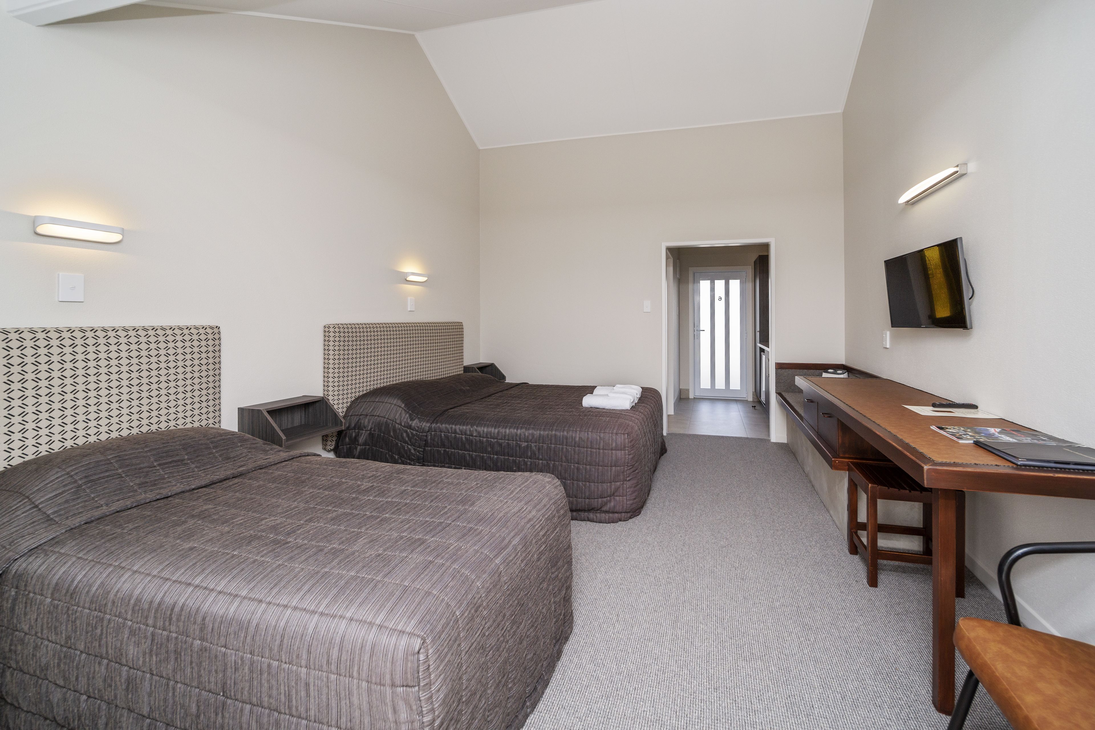 A hotel room with two beds, a desk, a chair, and a TV on the wall.