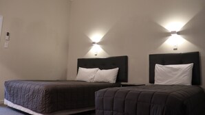 A hotel room with two beds, each with a dark headboard and white pillows, and wall-mounted lighting.