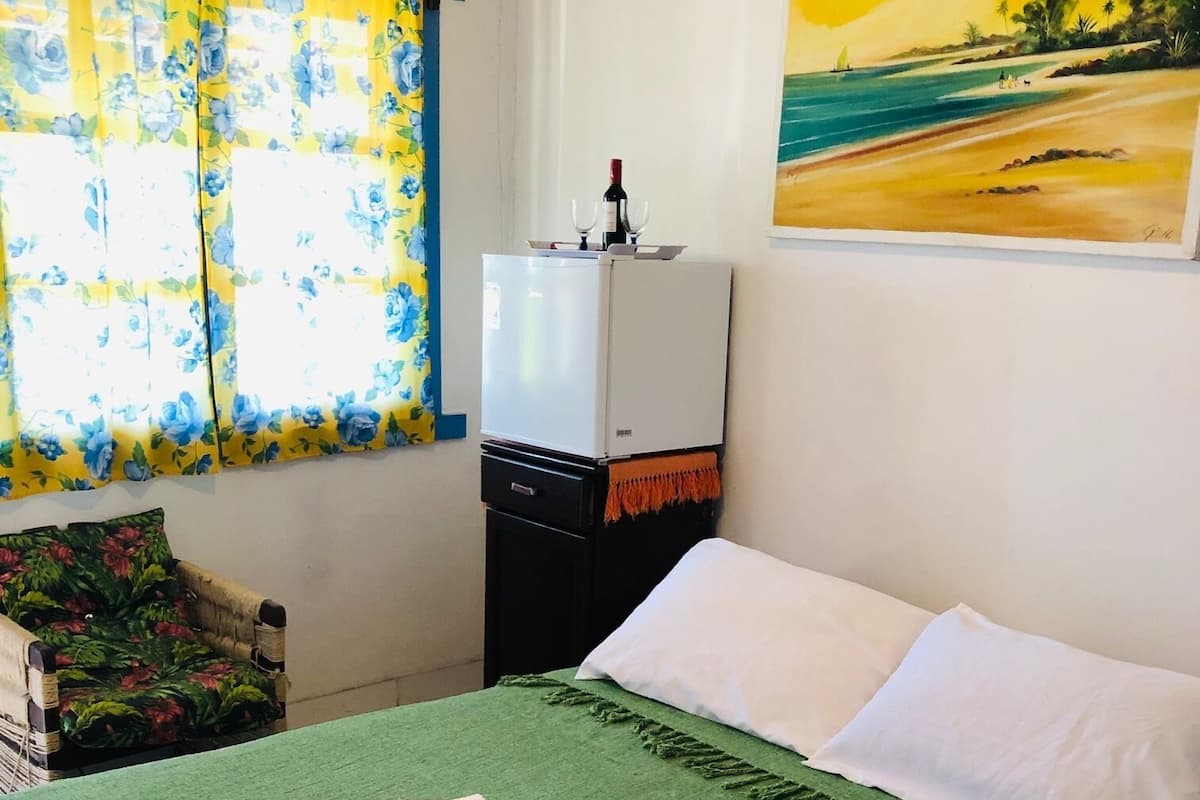 A hotel room with a bed, a refrigerator, a painting, and a window with curtains.