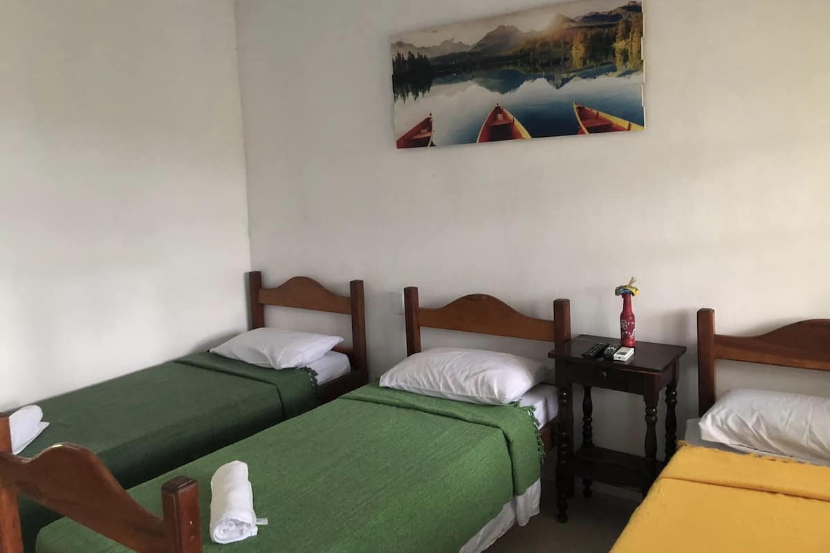 A hotel room with two single beds, a small table with a telephone, and a painting of a lake scene on the wall.