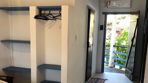 Una habitación de hotel con cama, una mesita, un estante y una puerta que da a un balcón.