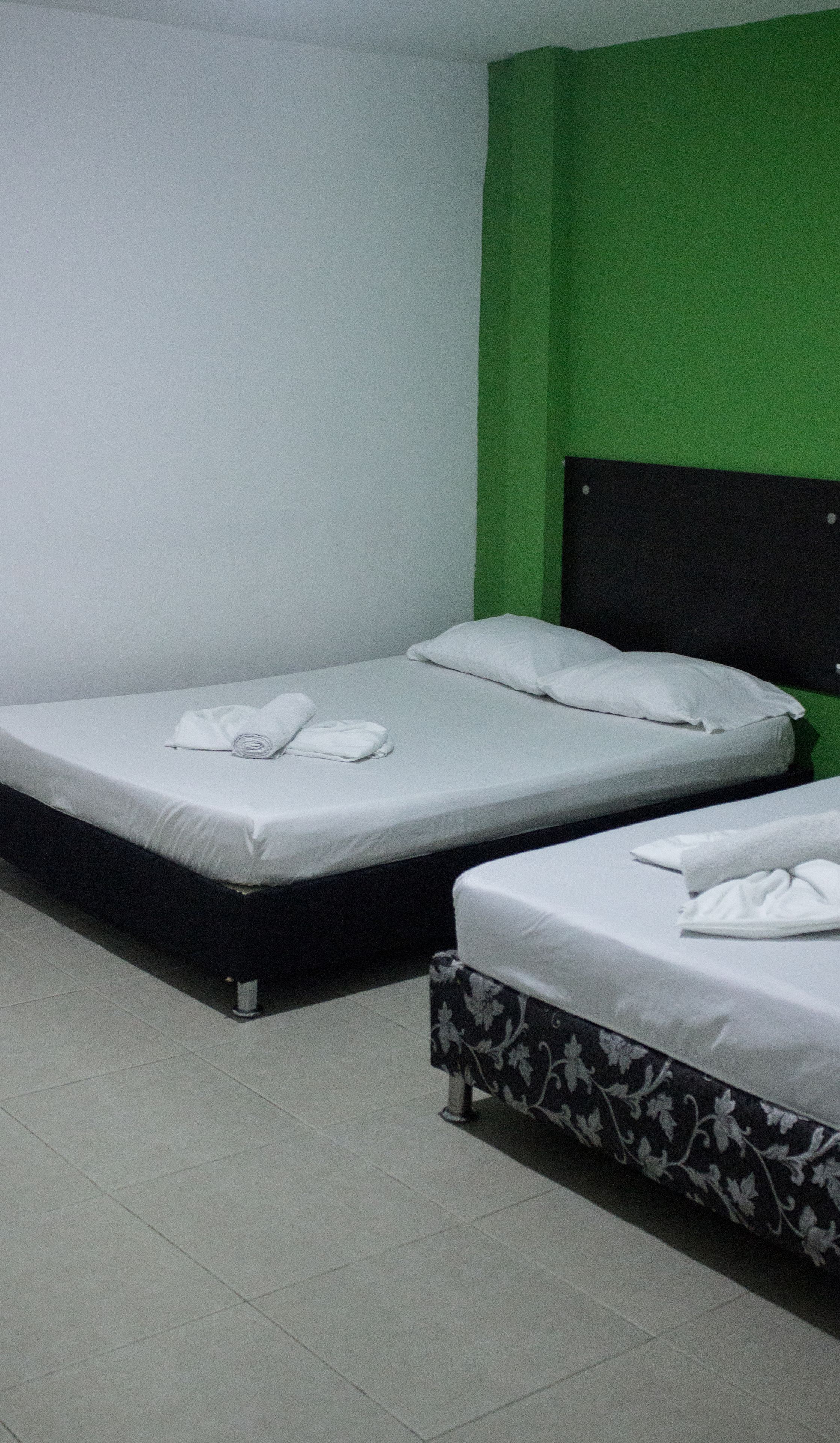 Quarto com duas camas, uma com cabeceira preta e outra com padrão floral.
