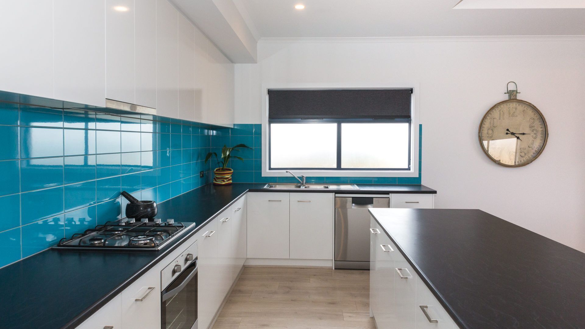 A modern kitchen with teal backsplash, white cabinets, a black countertop, and a stainless steel dishwasher.