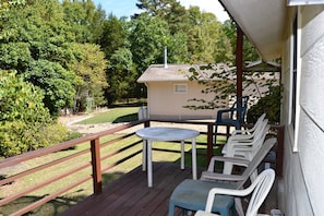 Relax on the covered deck with a round table and comfortable seating, surrounded by lush trees and a serene lawn.