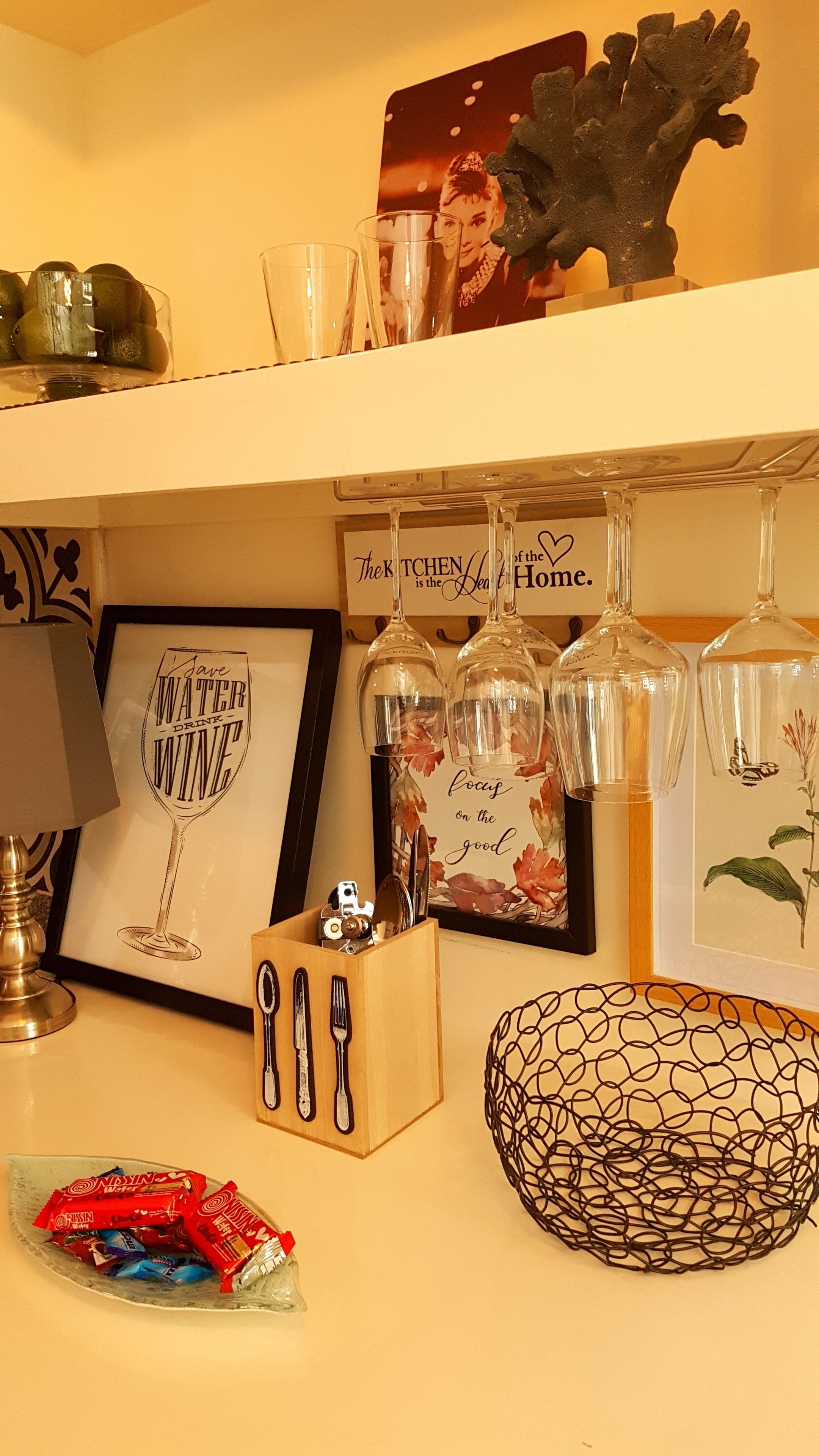 A kitchen counter with a framed quote, a wine glass, a knife block, a decorative bowl, and a picture frame.