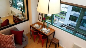 Un coin repas avec une table dressée pour quatre personnes, un miroir et une vue sur la rue grâce à de grandes fenêtres.