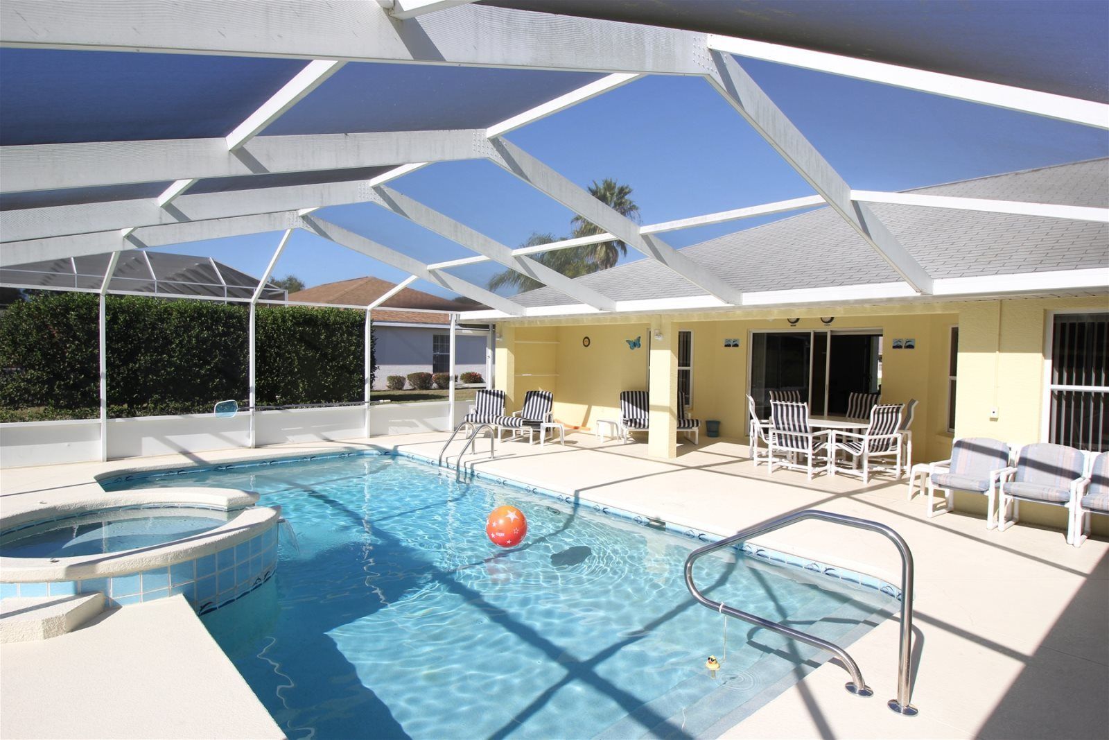 Une piscine avec un jacuzzi, entourée de chaises longues et dotée d’un patio couvert.