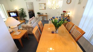 A dining area with a wooden table, chairs, a vase of flowers, a television, and a sofa. - Villa Lovie - Comfort - 4 Bedroom (Inverness)