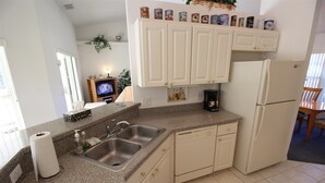 A compact kitchen with a granite countertop, stainless steel sink, and white cabinetry. A coffee maker and a small television are visible on the counter. - Villa Lovie - Comfort - 4 Bedroom (Inverness)
