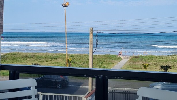 A balcony with a view of the ocean, a table, and chairs.
