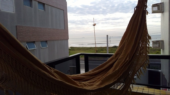 A hammock on a balcony overlooking a beach with buildings in the background.
