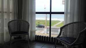 A balcony with two wicker chairs, a view of the sea, and a tiled floor.