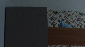A hotel room with a bed, a bedside table with a lamp, and a patterned wall above the bed.
