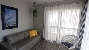 A living room with a sofa, a chair, a framed picture, and sheer curtains.