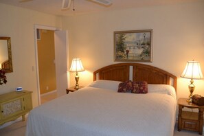 A hotel room with a large bed, two bedside tables with lamps, a painting above the bed, and a door leading to another room.