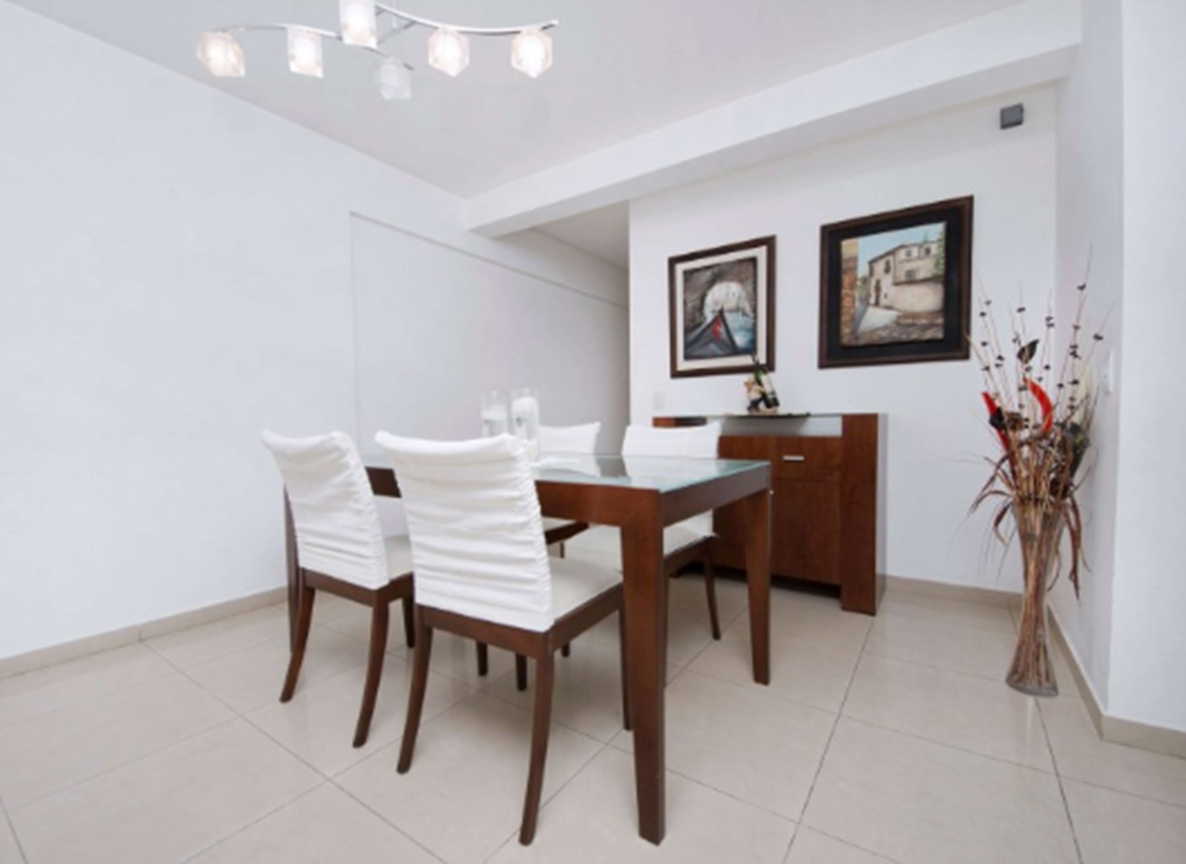A dining area with a wooden table and chairs, a white cabinet, and two framed pictures on the wall.