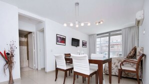Een moderne woonkamer met een eethoek, een bank, een televisie en een groot raam.