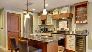 A modern kitchen with a central island, stainless steel appliances, and wooden cabinetry. - Aurora 225 | Resort Suite with Pool & Hot Tub (Canmore)