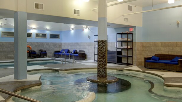 A pool area with a hot tub, lounge chairs, and a seating area with a sofa. - Aurora 225 | Resort Suite with Pool & Hot Tub (Canmore)