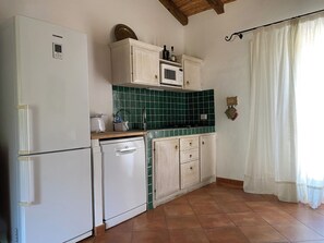 A kitchen with a white refrigerator, a dishwasher, a microwave, and a cabinet with bottles on top.