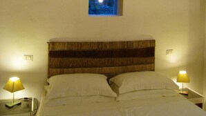 Ein Schlafzimmer mit einem hölzernen Kopfteil, zwei Nachttischlampen und einem kleinen Fenster mit Blick auf eine nächtliche Szene.
