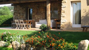 Ein Steinhaus mit überdachter Terrasse, Sitzgelegenheiten im Freien und einem Garten mit Blumen.