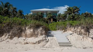 Ein Strandgrundstück mit einer Treppe, die zu einem von Palmen und Vegetation umgebenen Gebäude führt.