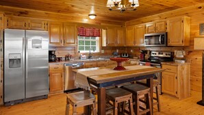 Cocina de cabaña de madera con un refrigerador de acero inoxidable, un microondas, una estufa, armarios de madera y una mesa de comedor de madera con taburetes.