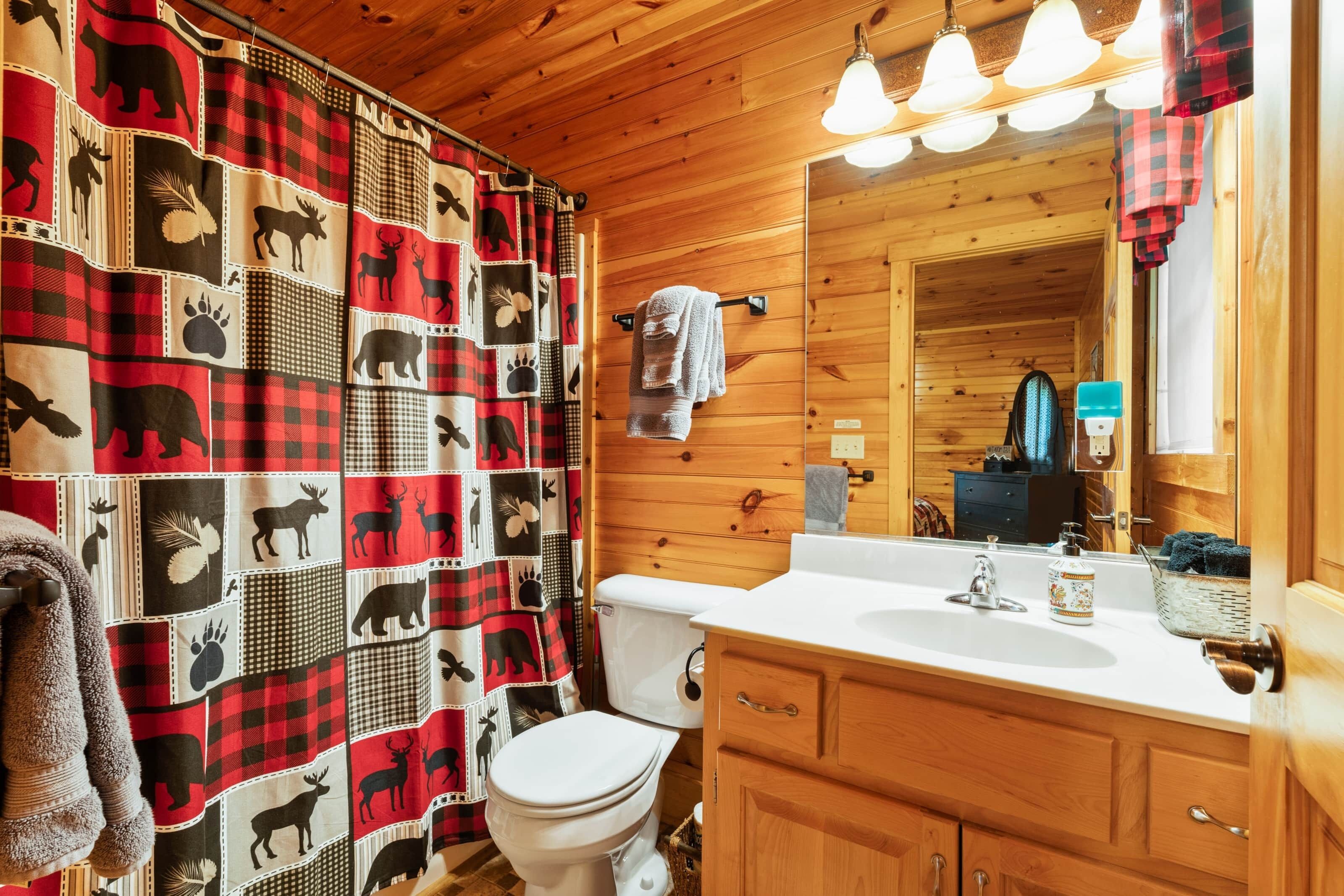 Un baño con cortina de ducha a cuadros, inodoro blanco, armarios de madera y lavabo con espejo.