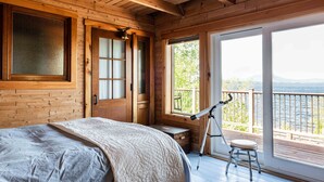 Une chambre dans un chalet en bois, avec un lit, un télescope et une vue sur un lac.