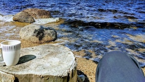 Une jetée en bois, sur laquelle se trouvent une tasse blanche et une paire de chaussures, donnant sur un lac bordé de rochers et surplombant des montagnes lointaines.