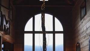 Un chalet confortable doté d’une grande fenêtre en arc de cercle donnant sur un plan d’eau, de murs en bois et d’un coin repas avec des chaises et une table.