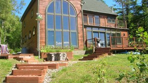 Une grande maison en bois, dotée d’une fenêtre en arc en plein cintre bien visible, d’un balcon et d’un élément décoratif en pierre dans le jardin avant.